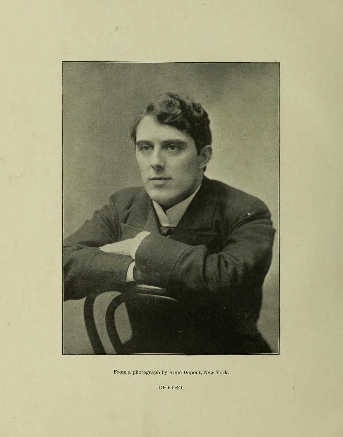 Black-and-white studio portrait of a young Cheiro in a dark suit, arms folded on the back of a chair