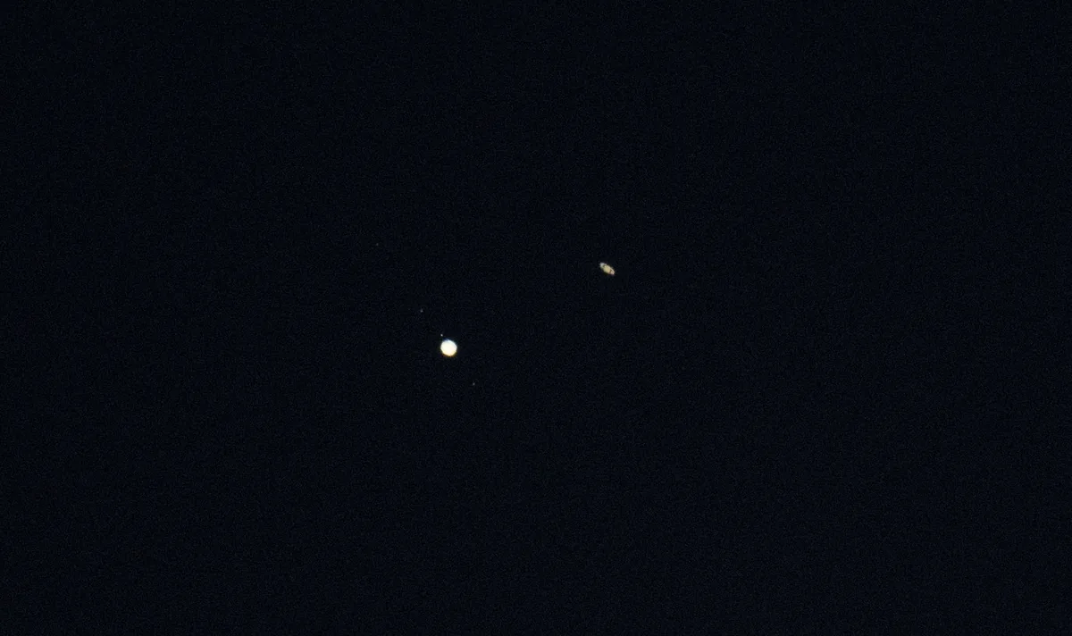 Telescope photo of bright Jupiter with small moons and ringed Saturn very close together in a dark sky