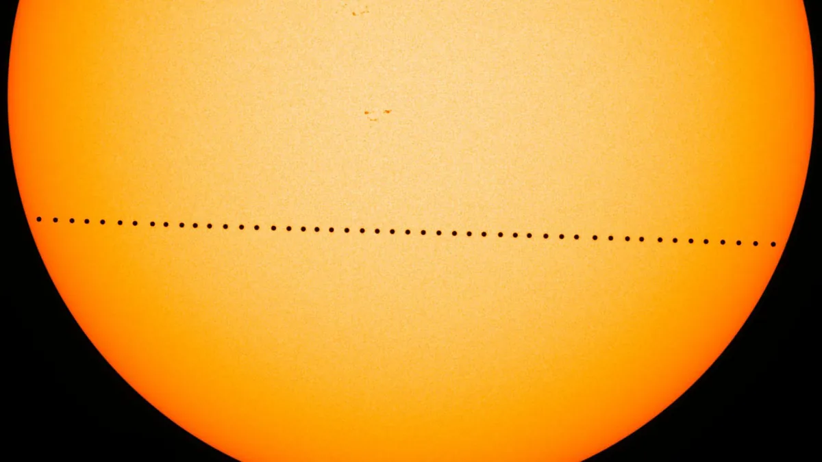 Composite image of the orange Sun with a line of small black dots showing Mercury crossing in front of it